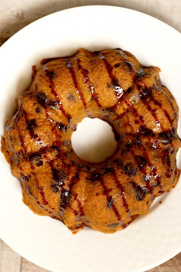 overhead shot of Instant Pot Chocolate Chip Bread from 365 Days of Slow Cooking and Pressure Cooking's review of Instantly Sweet Dessert Cookbook - featuring a white plate holding a golden brown bundt cake dotted with chocolate chips and drizzled with additional chocolate sauce