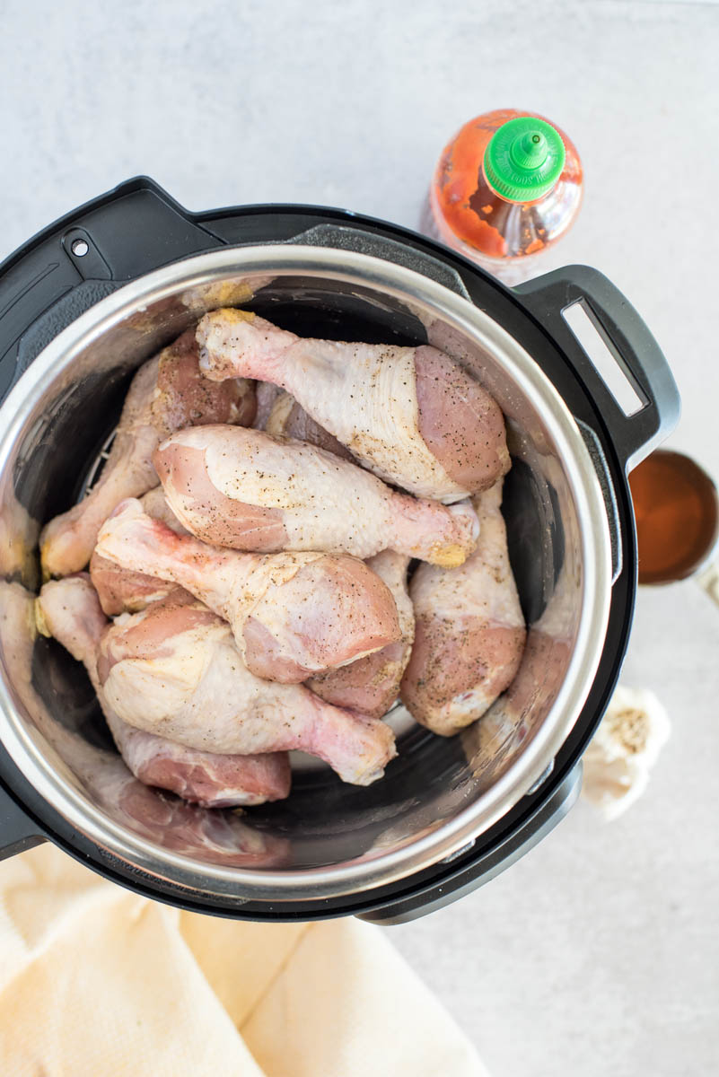 Overhead picture of raw chicken drum sticks ready to cook in an Instant Pot with Sriracha sauce in the background.