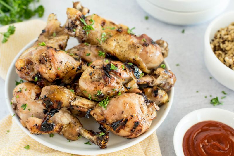 A plate of Instant Pot honey Sriracha chicken drum sticks placed next to dipping sauce with fresh parsley in the background.