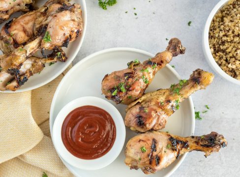 Instant Pot honey Sriracha chicken drumsticks on a plate, next to BBQ sauce.