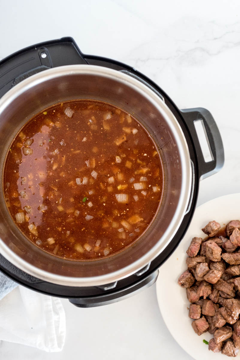 An overhead shot looking down into an Instant Pot filled with broth and ready to add the stroganoff back in