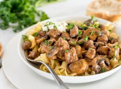 a horizontal shot of beef stroganoff with a fork on the left-hand side, with mushrooms visible garnished with black pepper and sour cream