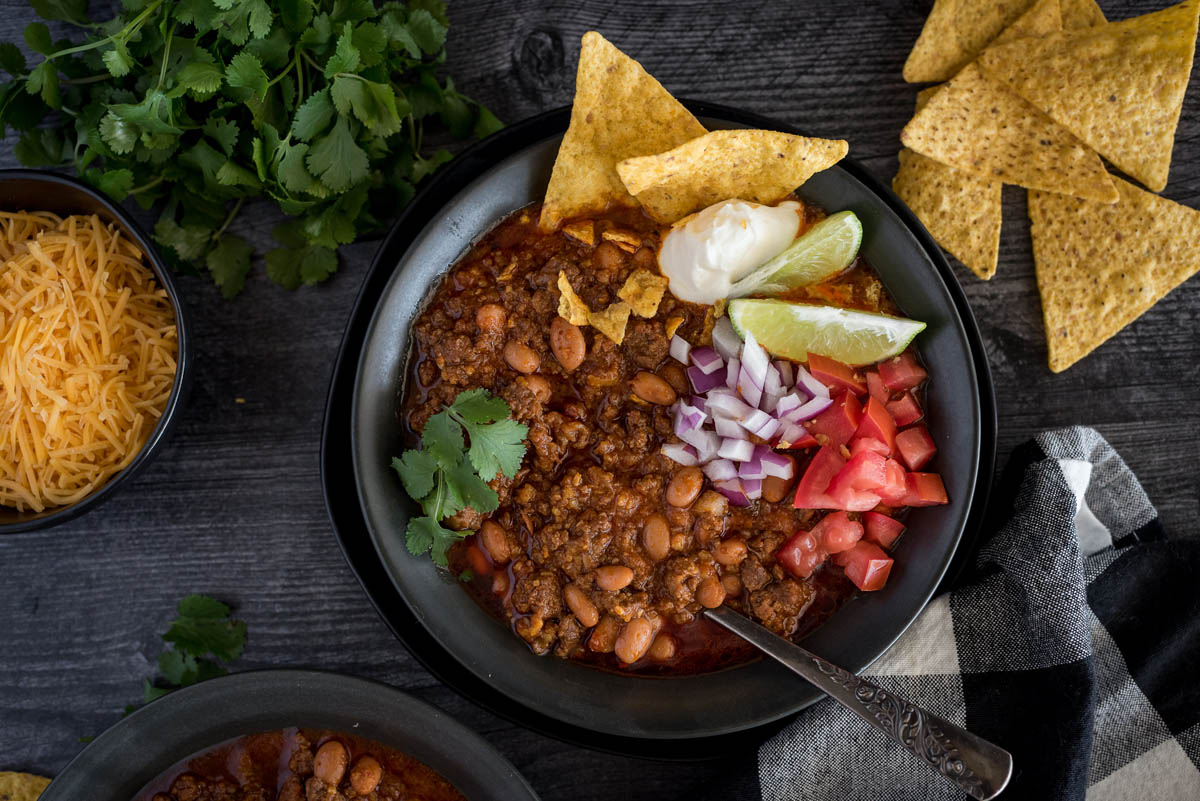 A bowl of Instant Pot chili topped with diced tomatoes, red onion. lime wedges, sour cream, and cilantro