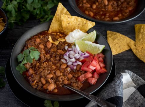 A bowl of Instant Pot chili topped with diced tomatoes, red onion. lime wedges, sour cream, and cilantro