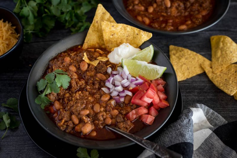 A bowl of Instant Pot chili topped with diced tomatoes, red onion. lime wedges, sour cream, and cilantro