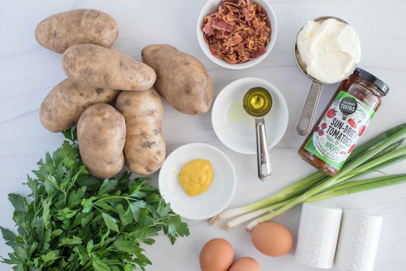 Ingredients for Instant Pot potato salad with bacon, including eggs, parsley, green onions, sun dried tomatoes, mayonnaise, mustard, bacon, and potatoes.