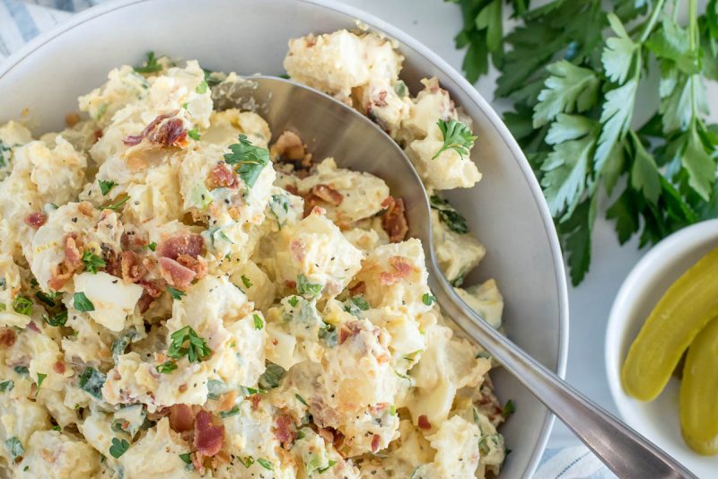 Close up picture of BLT potato salad made in an Instant Pot, with fresh parsley and sliced pickles in the background.