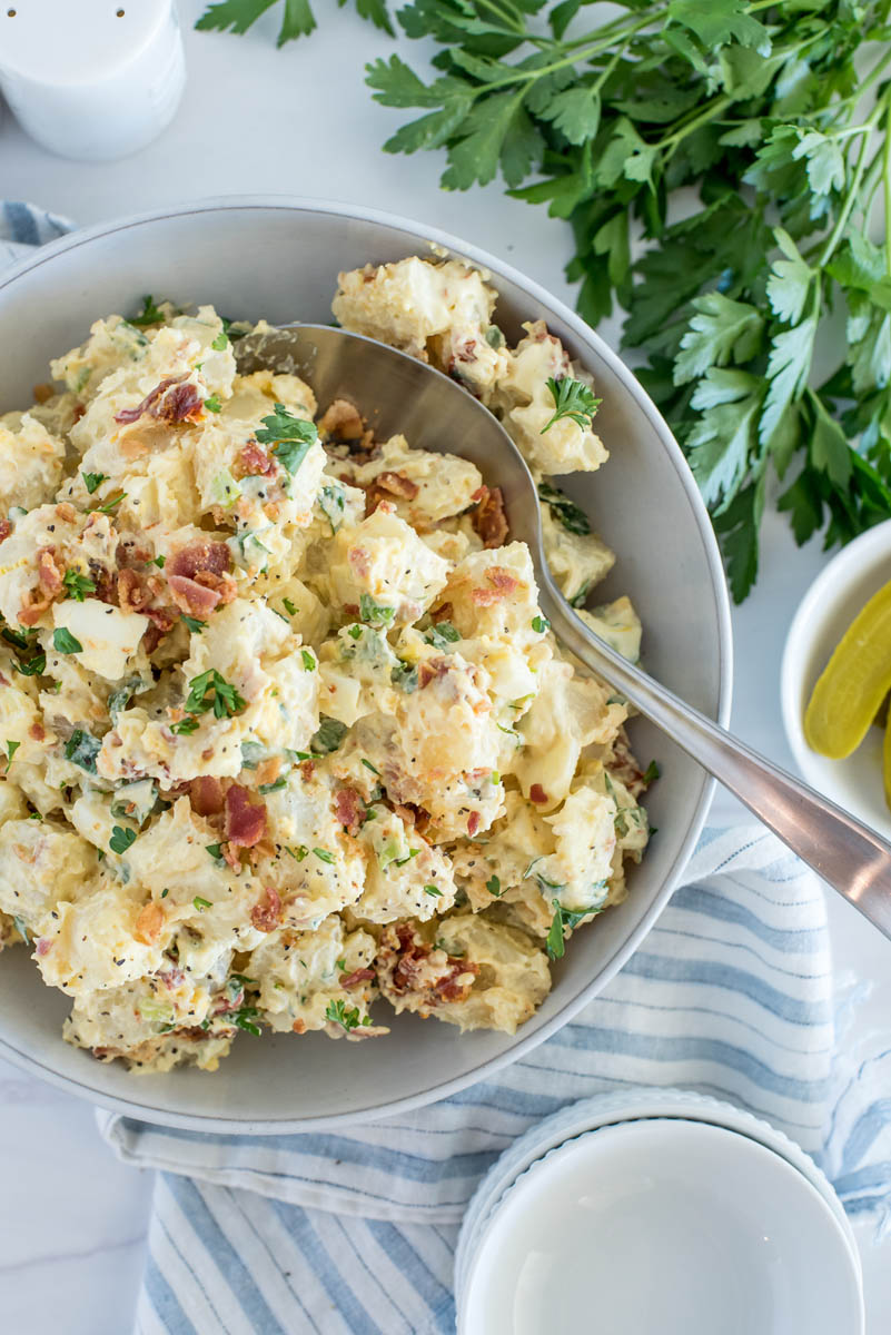 Overhead picture of Instant Pot potato salad with bacon and tomatoes added, with parsley and pickles in the background.