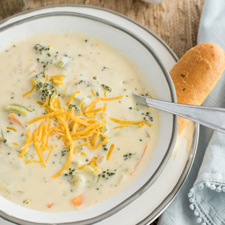 Pressure Cooker Broccoli Cheese Soup close up topped with cheese and served with a breadstick