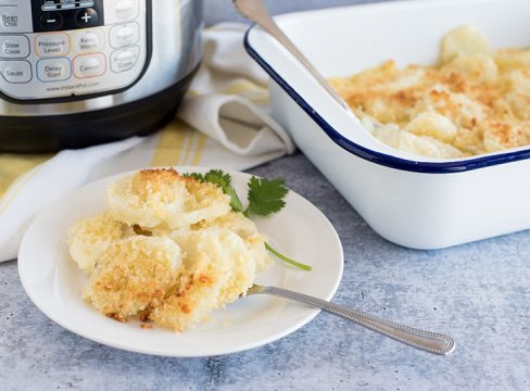 Instant Pot Scalloped Potatoes, plated on a small white plate with an Instant Pot Duo and a white baking dish in the background