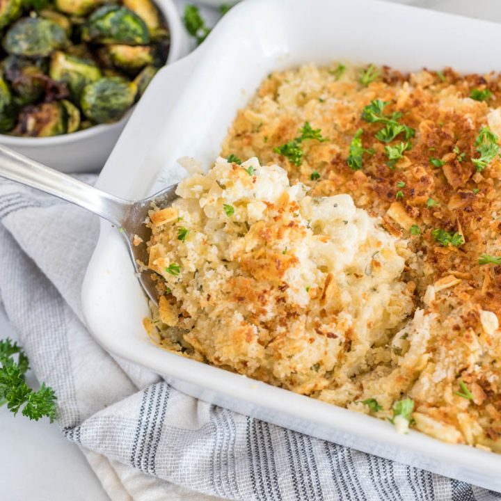 Close up shot of Instant Pot hash brown casserole been scooped from a serving dish with roasted Brussel sprouts in the background.