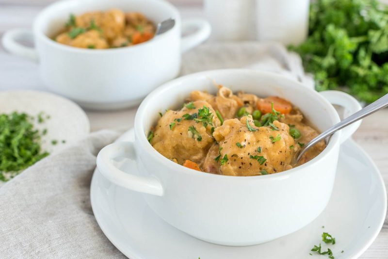 Close up picture of a white bowl with Instant Pot chicken and dumplings, with fresh parsley and another bowl of chicken and dumplings in the background.