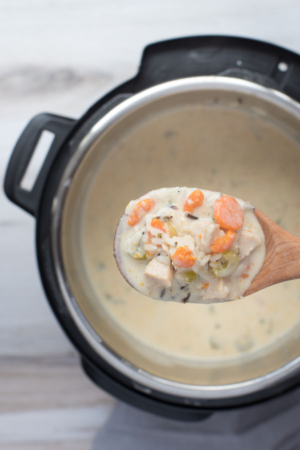 Overhead of a close up on creamy pressure cooker chicken wild rice soup on a wooden spoon with carrots, wild rice, chicken, celery and creamy broth.