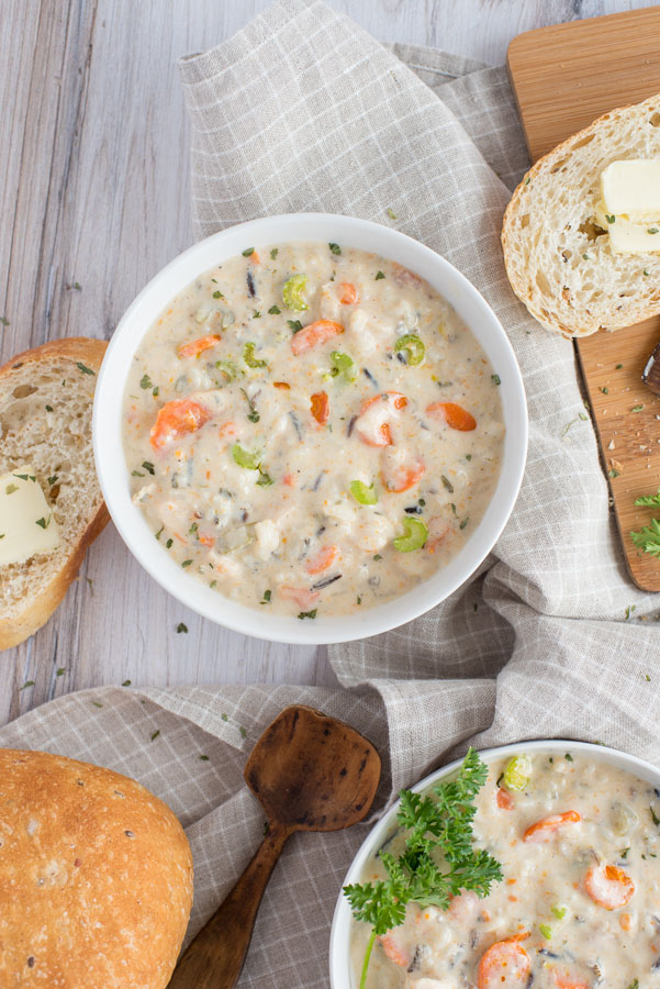 Overhead of two white bowls full of creamy pressure cooker chicken and wild rice soup with crusty white bread and butter on a checkered cloth napkin.