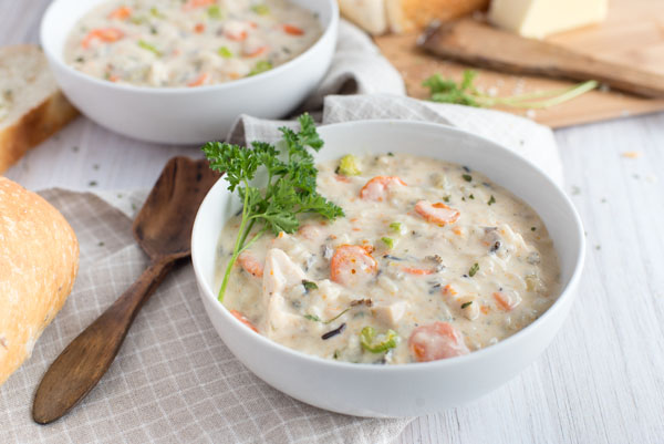 two white bowls filled with creamy Instant Pot chicken wild rice soup garnished with parsley on a grey checkered cloth napkin with a wooden spoon.