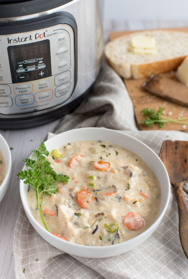 45 degree overhead of a white bowl full of chicken wild rice soup with an Instant Pot and crusty white bread and butter in the background.