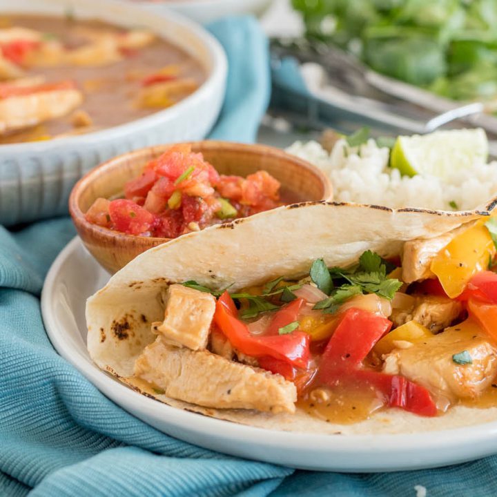 A side shot of Instant Pot Chicken Fajitas with a bowl of fajita filling in the background