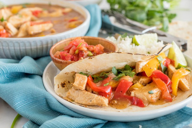A side shot of Instant Pot Chicken Fajitas with a bowl of fajita filling in the background