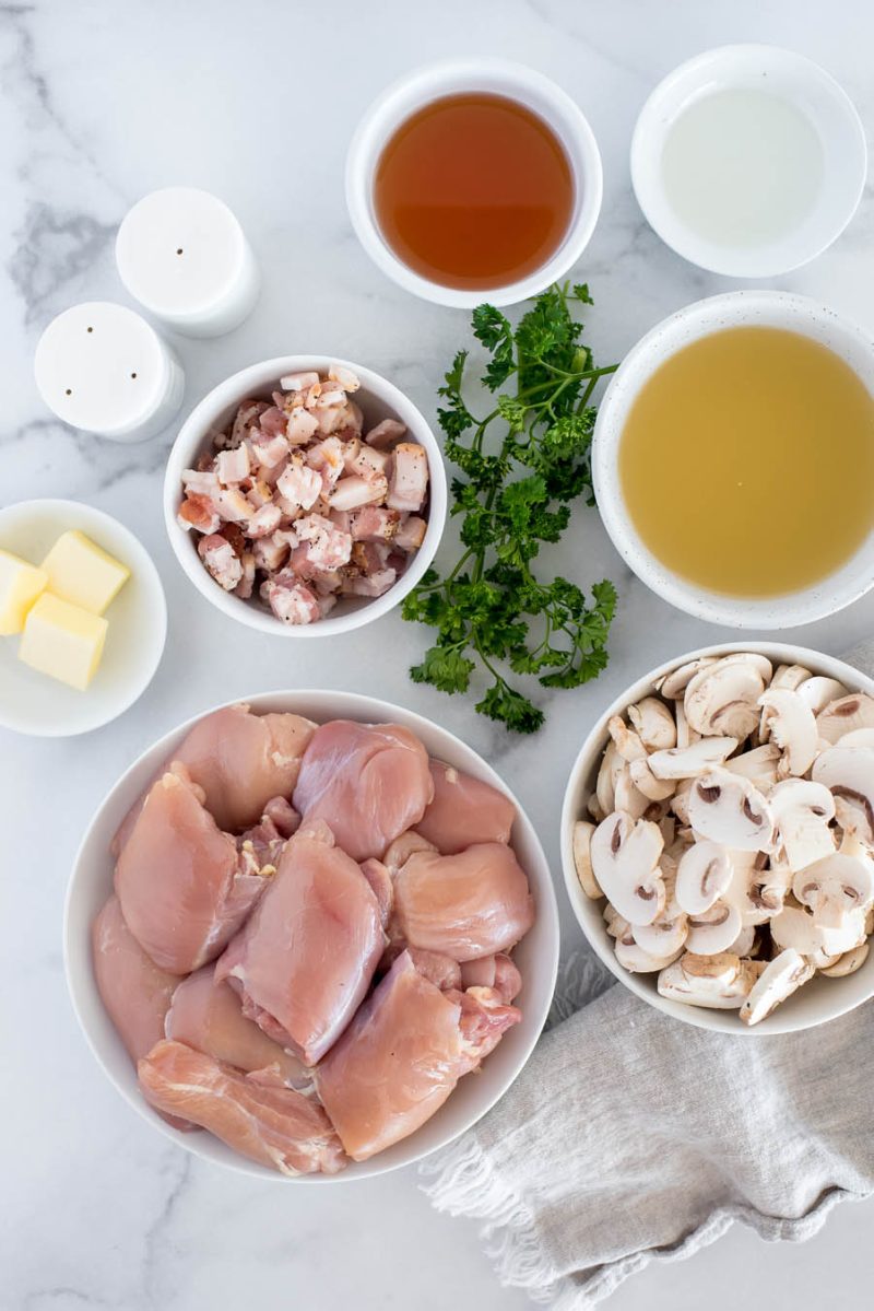 An overhead shot of the ingredients needed to make Instant Pot Chicken marsala, including chicken breasts, mushrooms, bacon, broth, butter, salt, and pepper