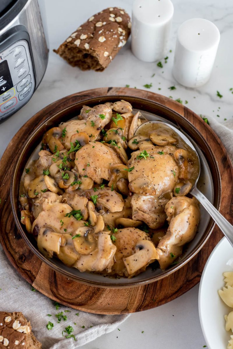 A high shot of a bowl full of Instant Pot chicken marsala in a dark bowl with an Instant Pot in the background