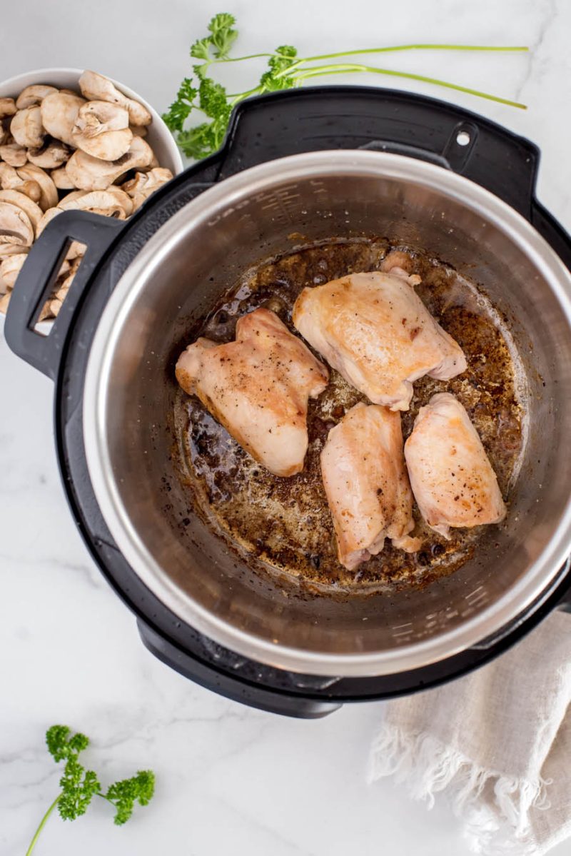 an overhead shot looking into the bottom of an Instant Pot filled with browned chicken thighs, ready to add the broth