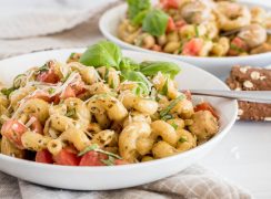 Side view of Instant Pot chicken pesto pasta served in a white bowl and topped with fresh basil and shredded parmesan.