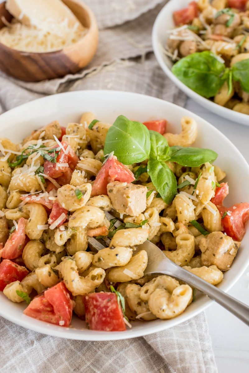 Close up shot of Instant Pot chicken pesto pasta in a white bowl and topped with fresh basil and parmesan cheese, with another bowl ready to serve in the background.