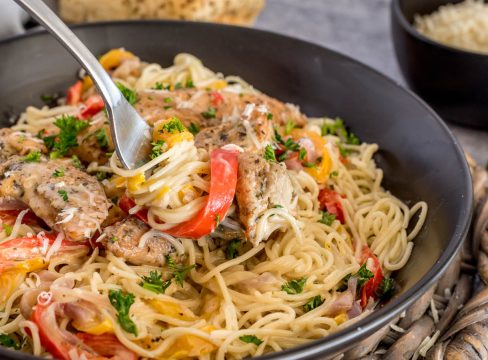 A fork with a twist of pasta noodles, with bell pepper and chicken ready to scoop into a bite