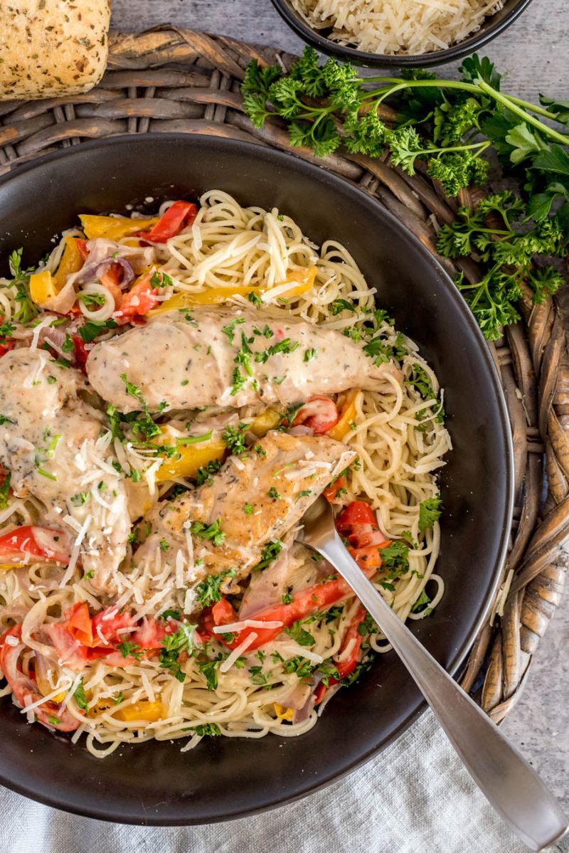 an overhead, close-up shot of a bowl of chicken scampi served with pasta and garnished with cheese and parsley