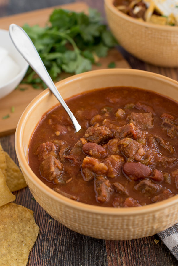 Close up of Pressure Cooker / Instant Pot Beef and Bean Chili with cilantro and sour cream in the background