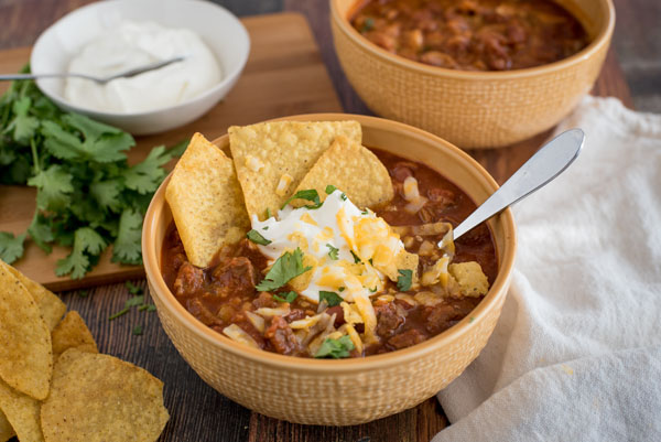 Beef and Bean Instant Pot Chili, dished up in a yellow serving bowl, topped with tortilla chips, sour cream, cheddar cheese, and cilantro