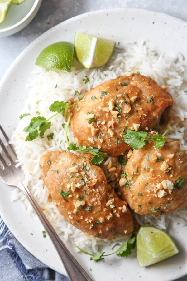 overhead shot of Instant Pot Thai Chicken from Completely Delicious's review of the Electric Pressure Cooker Cookbook - featuring a white plate with white rice, the thai chicken topped with diced cilantro and peanuts, with lime wedges for garnish
