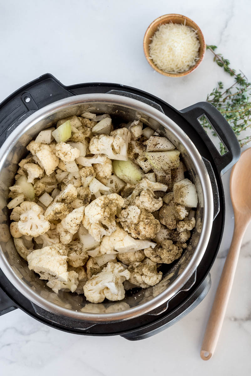 an overhead shot showing all of the ingredients inside an Instant Pot, including chopped cauliflower, spices, onions, and broth