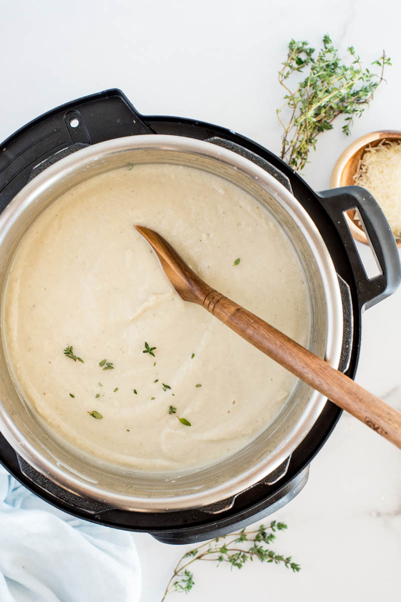 an overhead shot looking into the cooking pot of an Instant pot with the freshly blended cauliflower soup topped with a light sprinkle of fresh thyme