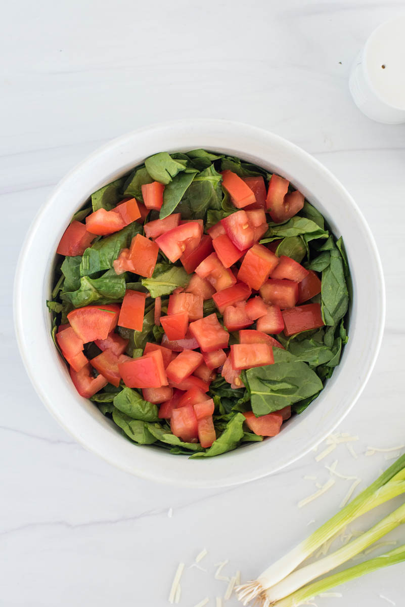 Chopped tomatoes mixed with spinach in a white bowl for Instant Pot crustless spinach quiche