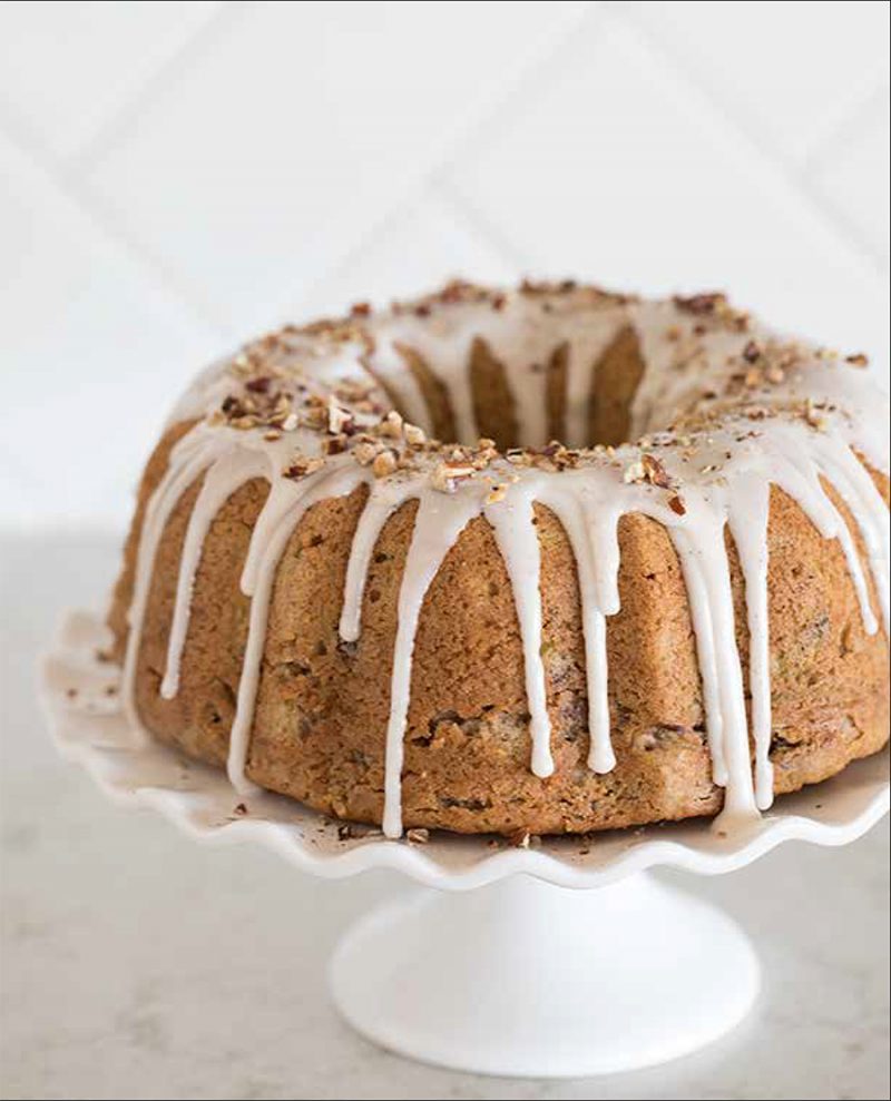 Cinnamon Zucchini Bread from the Electric Pressure Cooker Cookbook - featuring a head-on shot of zucchini bread made in a bundt pan with white cinnamon icing drizzled in drips down the sides and crushed nuts sprinkled around the top