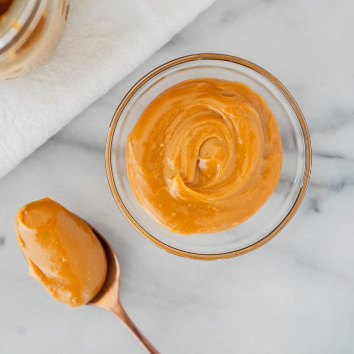 Dulce de leche in a bowl with a spoon next to it and a mason jar with more dulce de leche behind it.