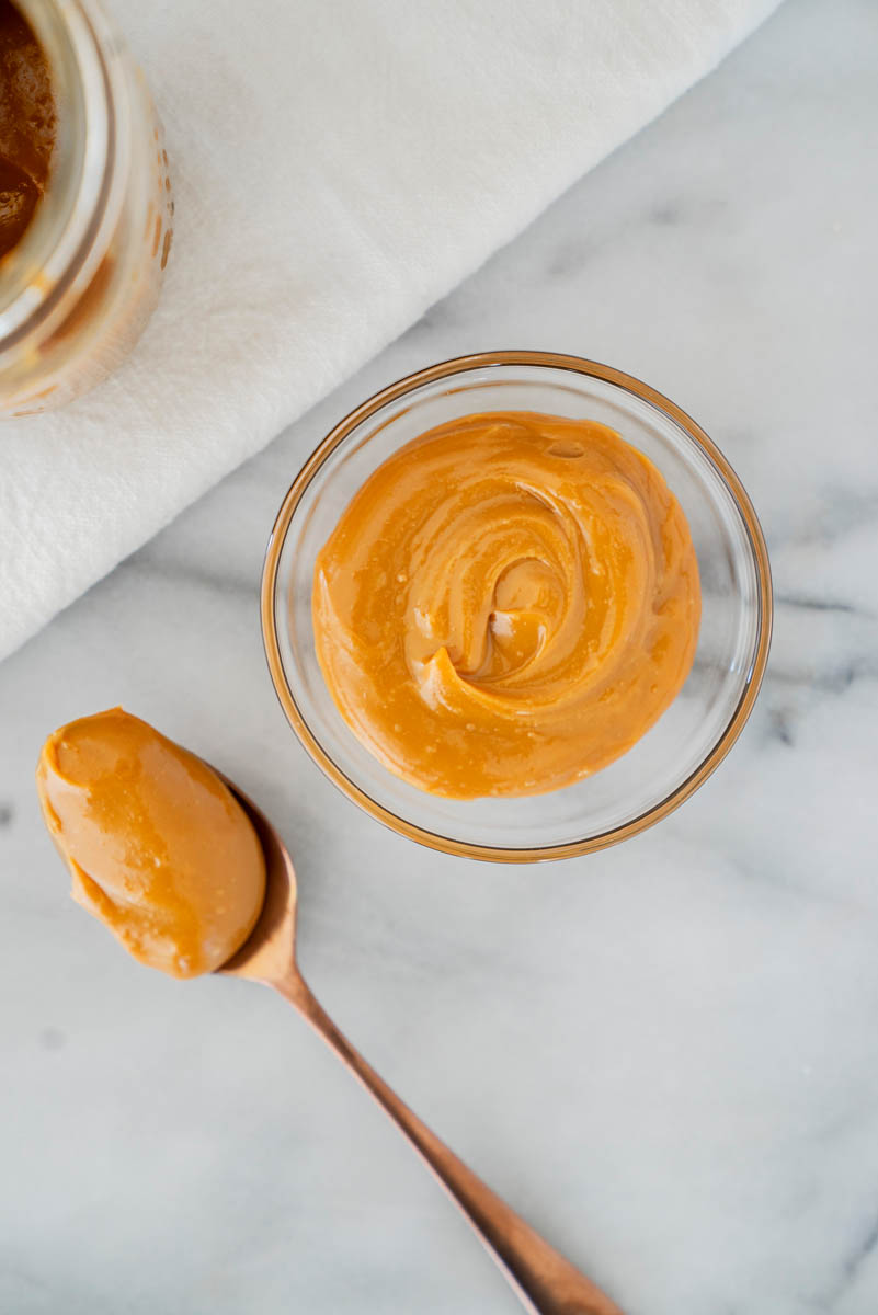 Dulce de leche in a bowl with a spoon next to it and a mason jar with more dulce de leche behind it.