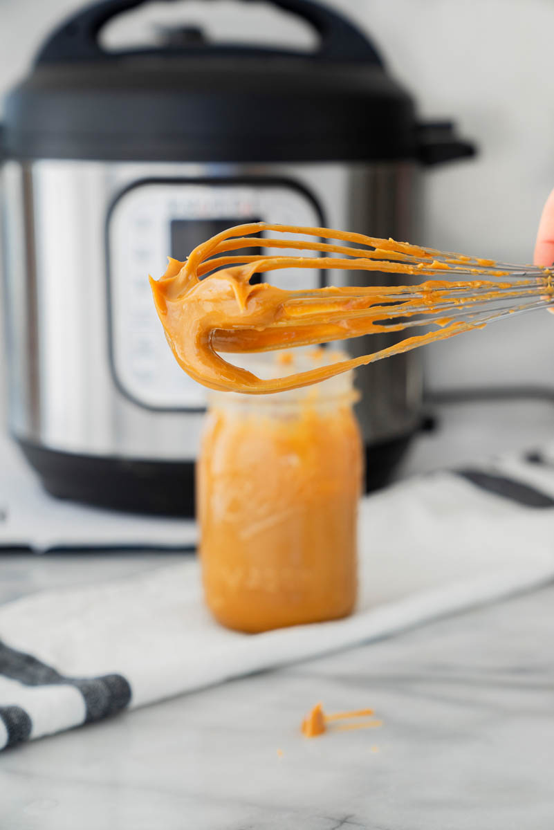 Dulce de leche on a whisk, with more in a mason jar, placed in front of an Instant Pot.