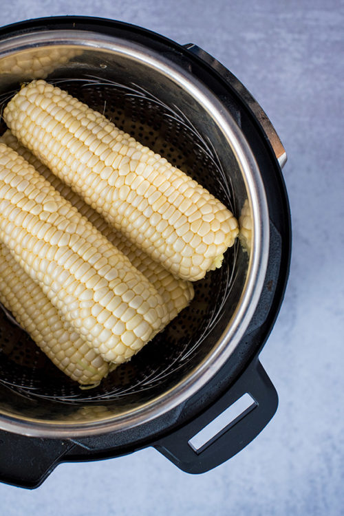 Pressure Cooker Corn on the Cob, husked and stacked on a steamer basket inside of an Instant Pot