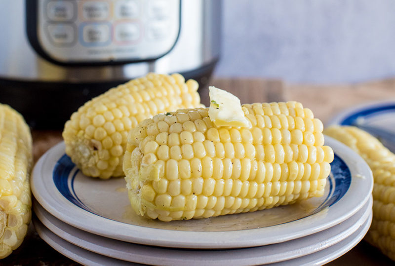 Easy Pressure Cooker Corn on the Cob, plated with an Instant Pot in the background