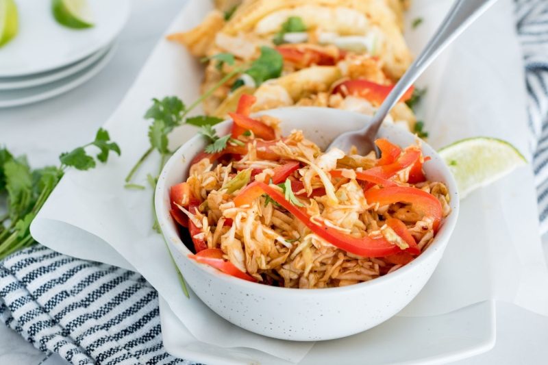 a bowl filled with shredded fish taco slaw and garnished with  limes and cilantro