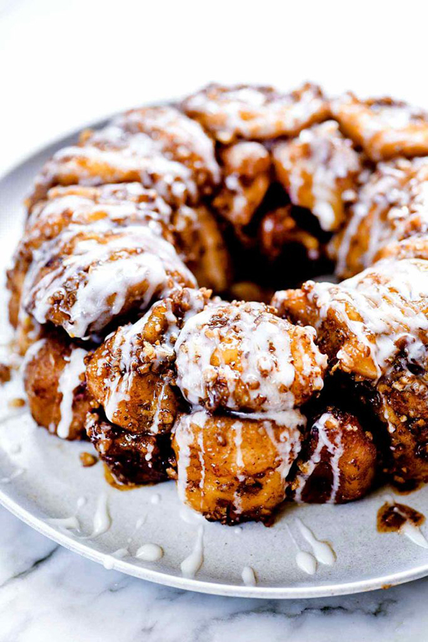 45 degree shot of Instant Pot Monkey Bread from Foodie Crush's review of Instantly Sweet dessert cookbook - featuring a white plate holding rounded balls of golden brown monkey bread bites, sprinkled with cinnamon and drizzled with white icing