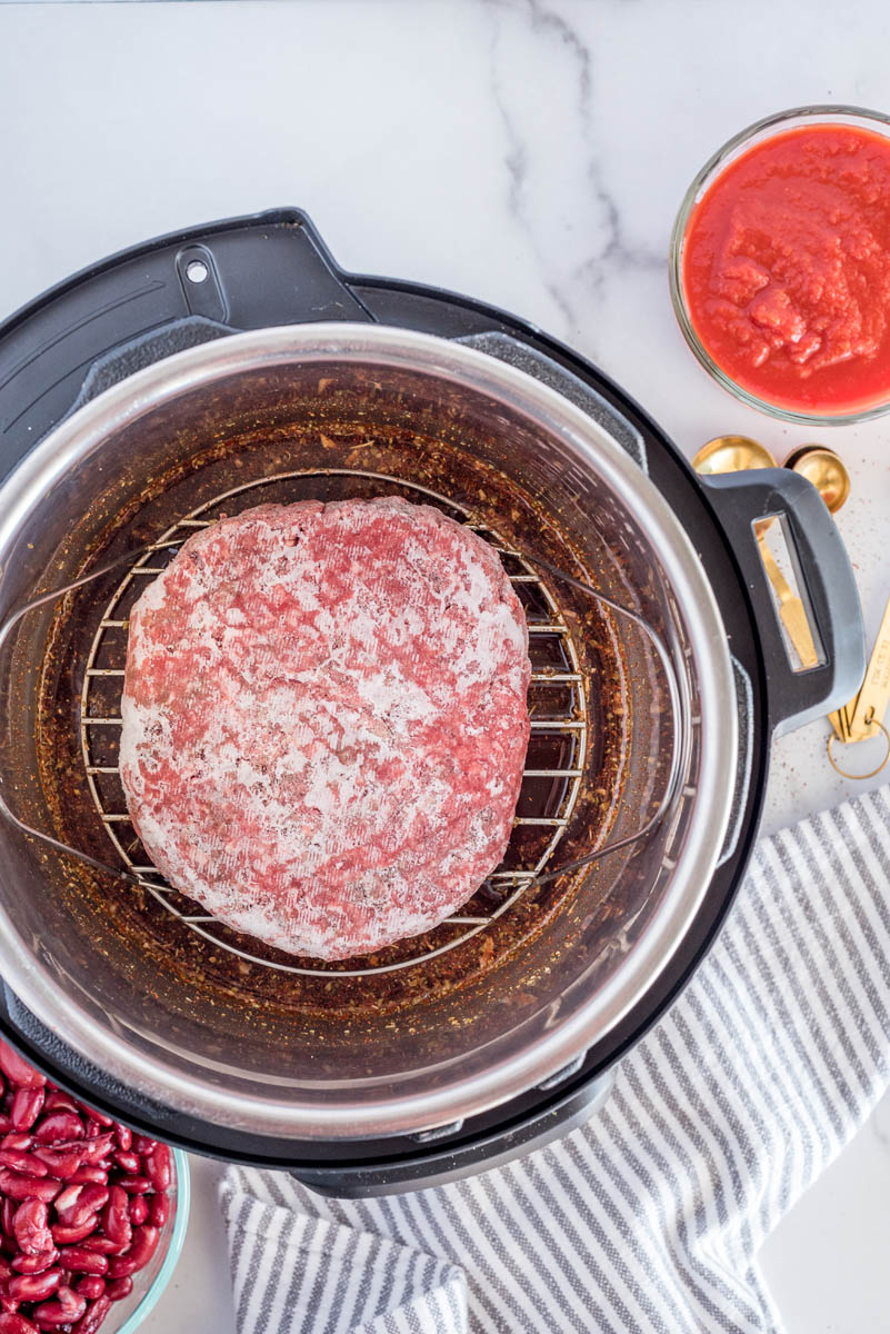 An overhead shot of Frozen Ground Beef on a trivet inside an Instant Pot cooking pot, with the tomatoes and kidney beans at the side
