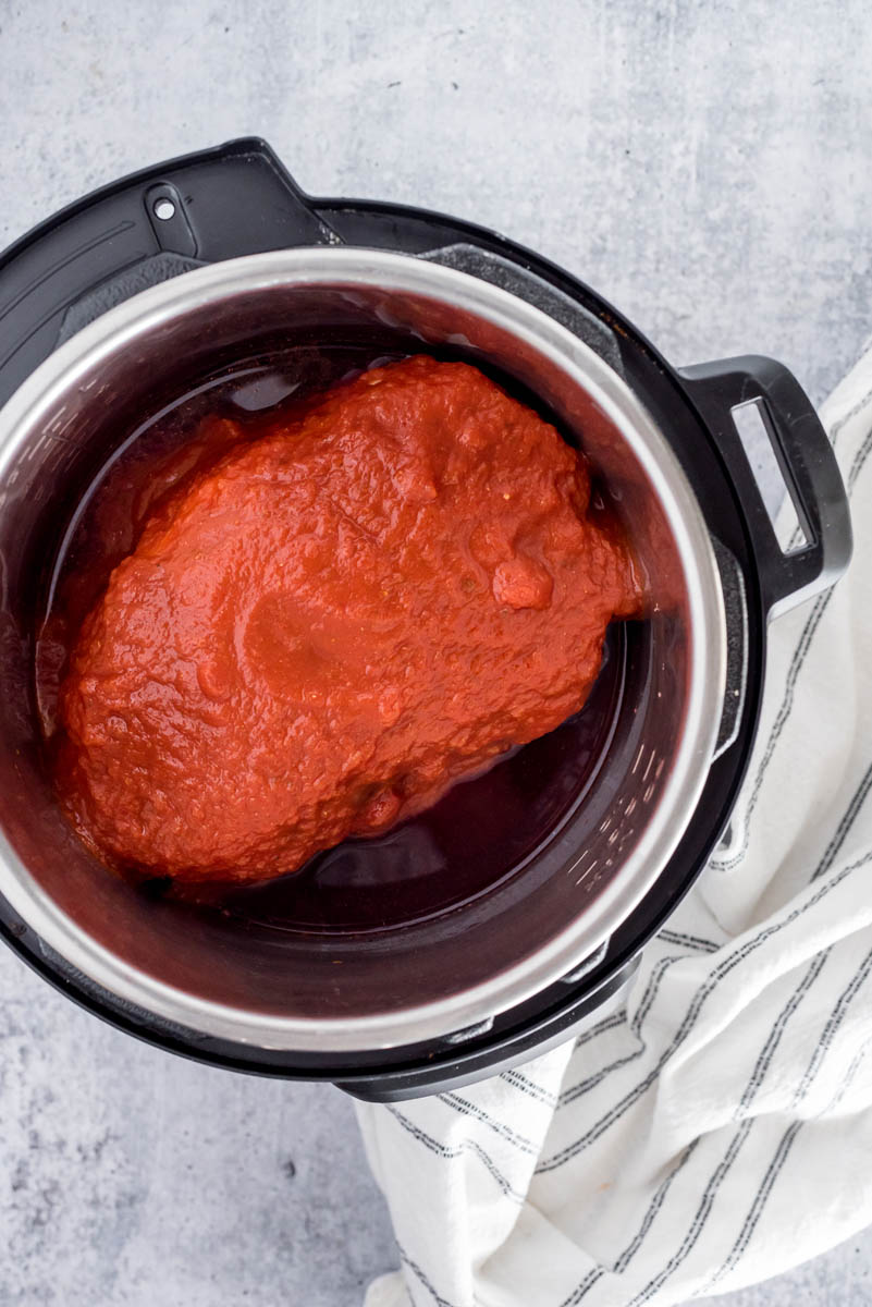 uncooked pot roast in a pressure cooker with marinara sauce