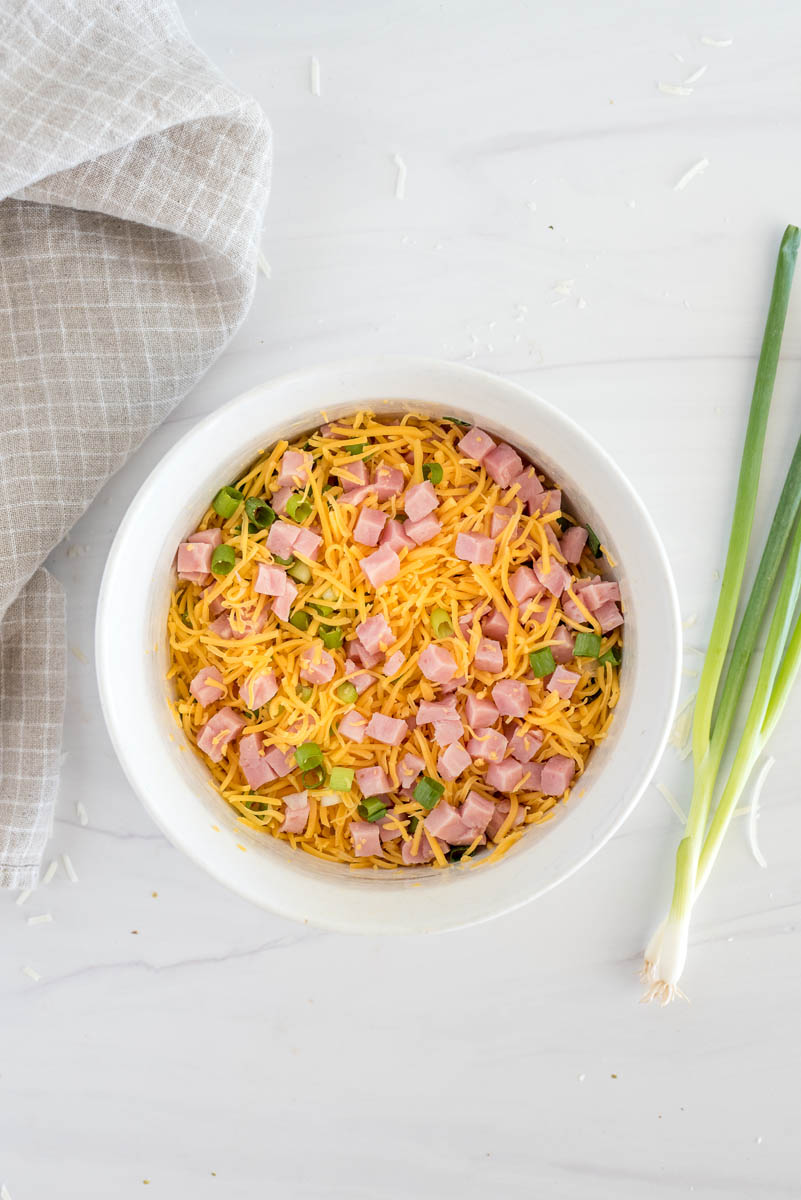 An overhead shot of the ham, cheese, and green onions in the bottom of a white soufflé round dish