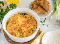 the finished and browned ham and cheese quiche in a white soufflé plan with toast and parsley in the background