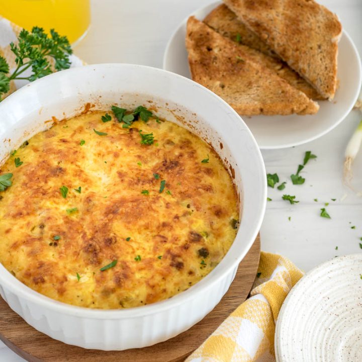 the finished and browned ham and cheese quiche in a white soufflé plan with toast and parsley in the background