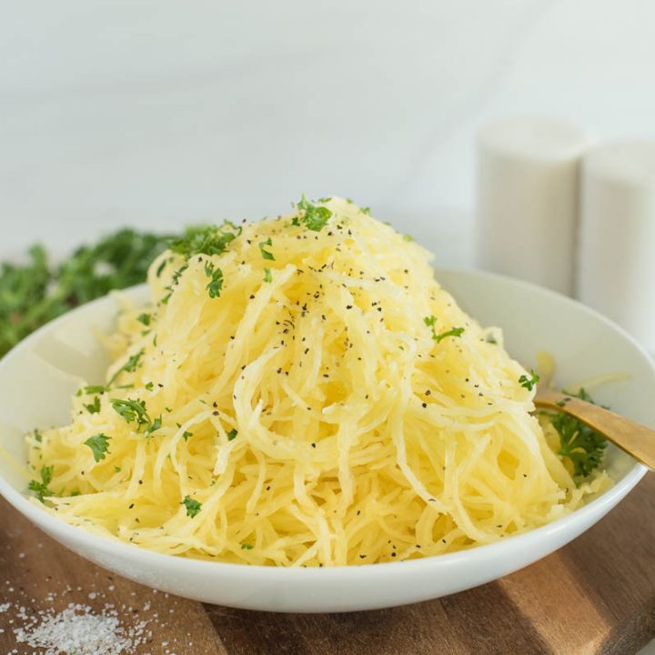 a horizontal shot of a bowl of spaghetti squash, garnished with parsley and sprinkled with salt and peper