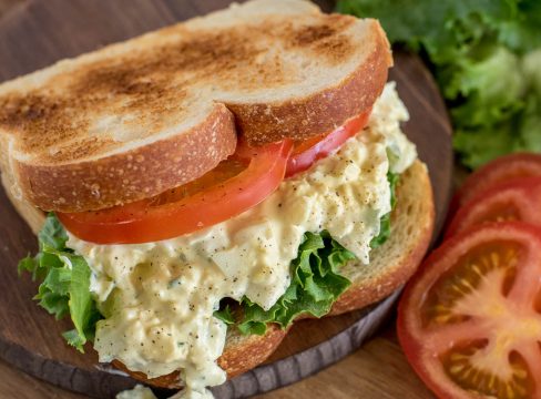 Close up picture of pressure cooker egg salad sandwich made with toasted bread, sliced tomato, and lettuce. Placed on a wooden cutting board.